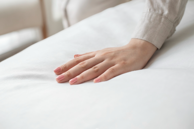 professionele-hotel-matras-topper-comfort Een hand die zachtjes op een wit, professioneel hotel topmatras drukt om het ligcomfort en de stevigheid te testen.