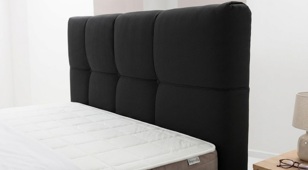 Zwart gestoffeerd hoofdbord met doorgestikt vakkenpatroon op een luxe hotelbed.